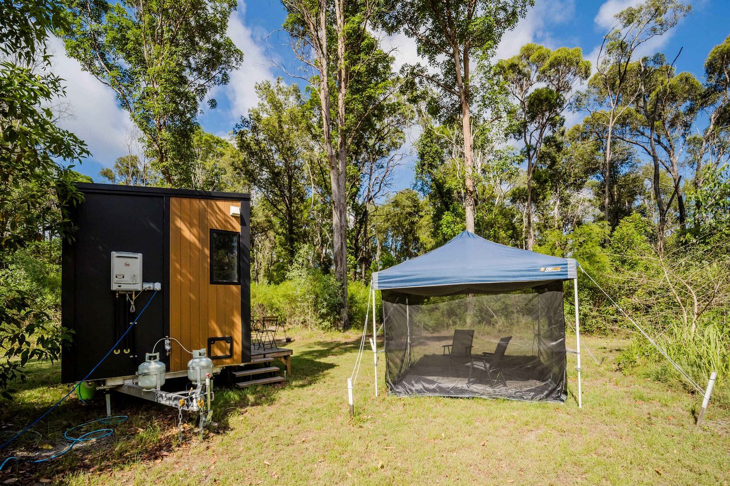 Montagem de camping com uma cabana de madeira pequena e uma tenda azul.
