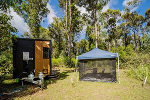 Montagem de camping com uma cabana de madeira pequena e uma tenda azul.