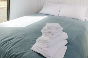 Un lit bien fait, avec une serviette blanche pliée posée sur le côté, une couvre-lit bleu clair et des oreillers blancs.