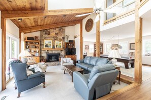 A spacious living room with a stone fireplace, wooden beams, and a high ceiling. - New Waterfront Retreat with Private Beach, Dock, Billiards & Parking on exclusive Thomas Point (Annapolis)