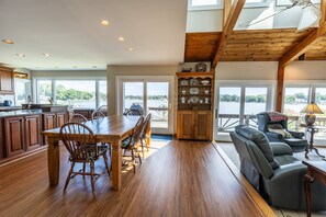 A spacious kitchen with wooden cabinets, a dining table with chairs, and a view of a body of water through large windows. - New Waterfront Retreat with Private Beach, Dock, Billiards & Parking on exclusive Thomas Point (Annapolis)