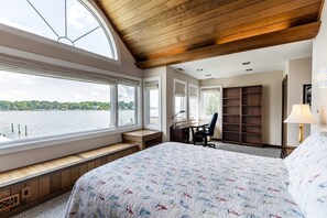 A bedroom with a large bed, a desk, and a chair, a bookshelf, and a view of a lake. - New Waterfront Retreat with Private Beach, Dock, Billiards & Parking on exclusive Thomas Point (Annapolis)