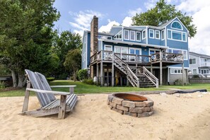 A two-story house with a deck and a fire pit in the foreground. - New Waterfront Retreat with Private Beach, Dock, Billiards & Parking on exclusive Thomas Point (Annapolis)