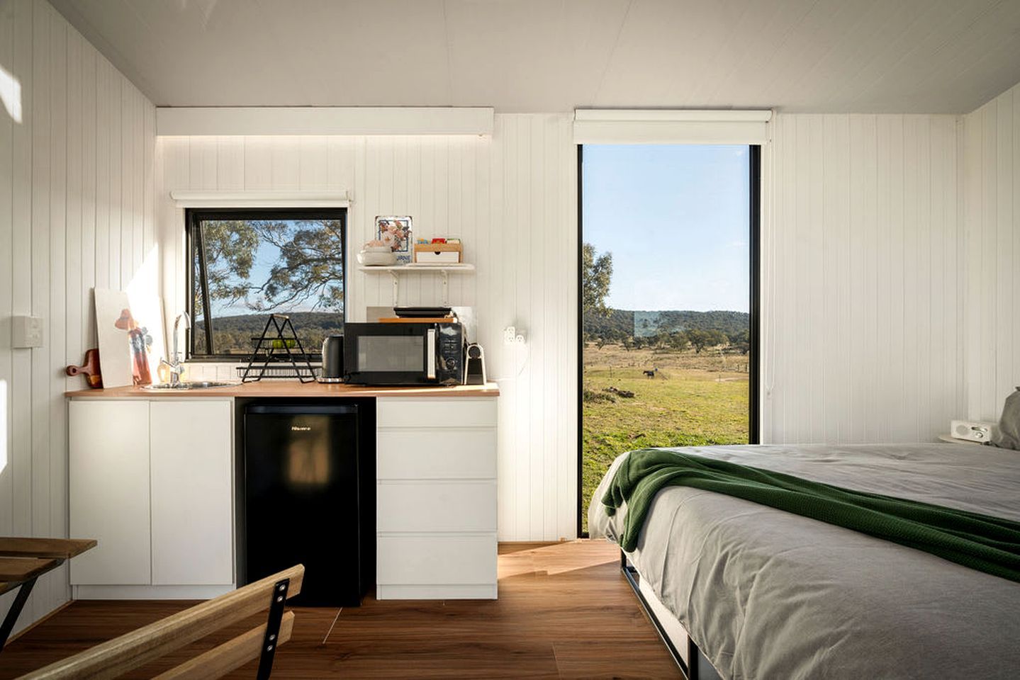 Un dormitorio compacto con cama, kitchenette pequeño y un ventanal que ofrece vistas a un paisaje rural.