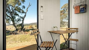 A room with a wooden table and chairs, a small potted plant, and a view of a rural landscape with trees and a fence.