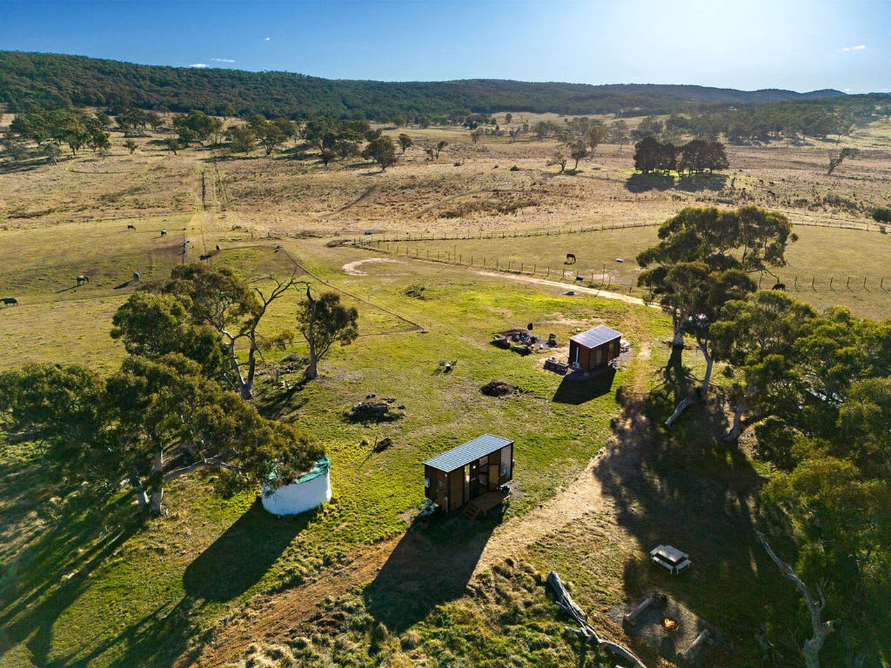 A rural landscape with a small cabin, a fenced area, and a white water tank.