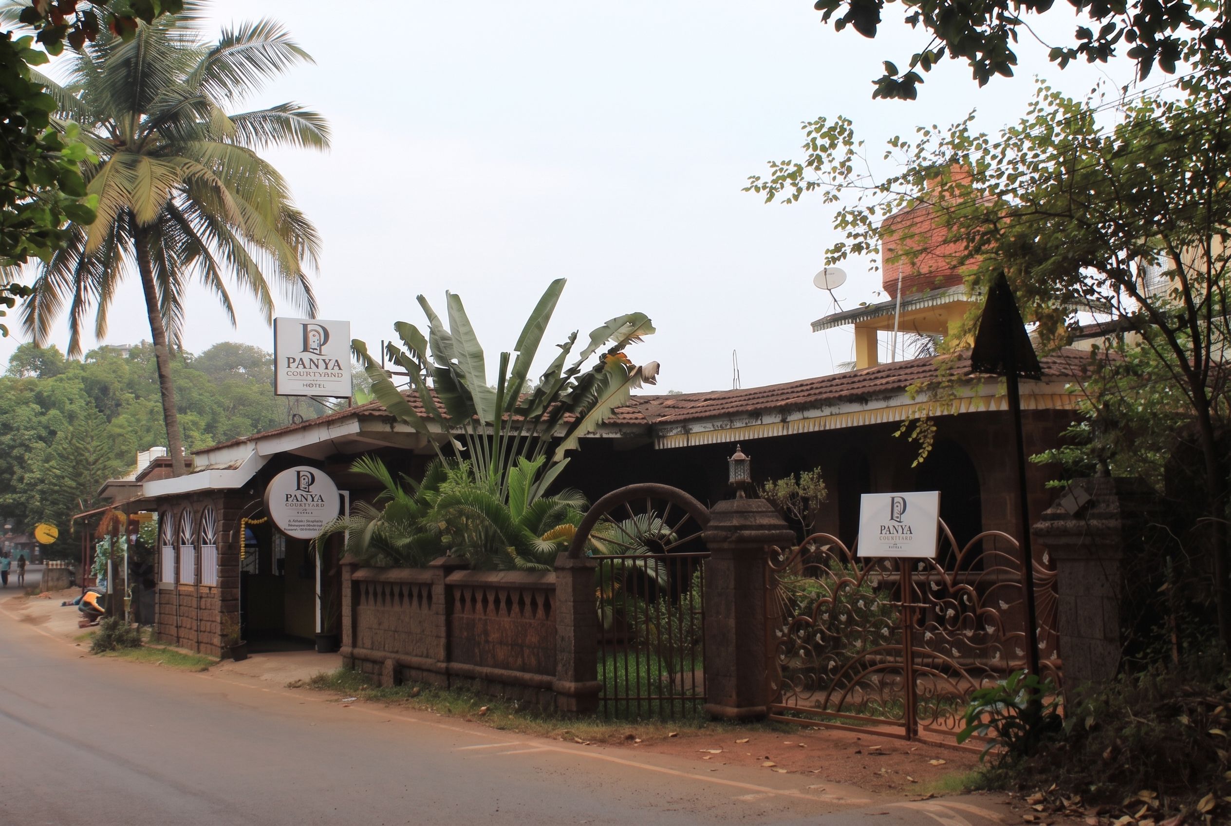 A hotel entrance with a sign reading 'Panya Courtyard Hotel' and a gated entrance with a wrought iron gate.