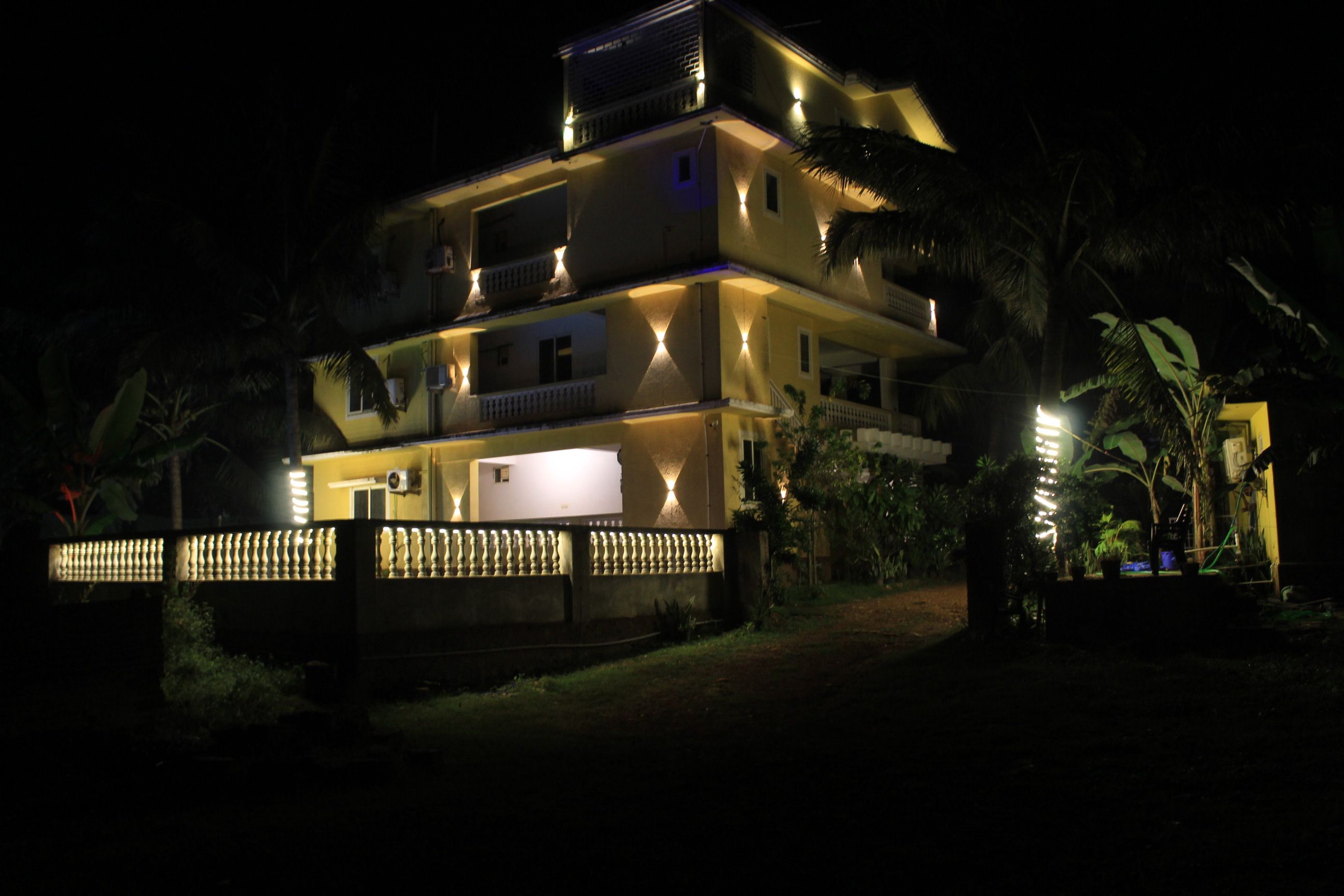 A multi-story building with balconies, a gated entrance, and surrounding vegetation.