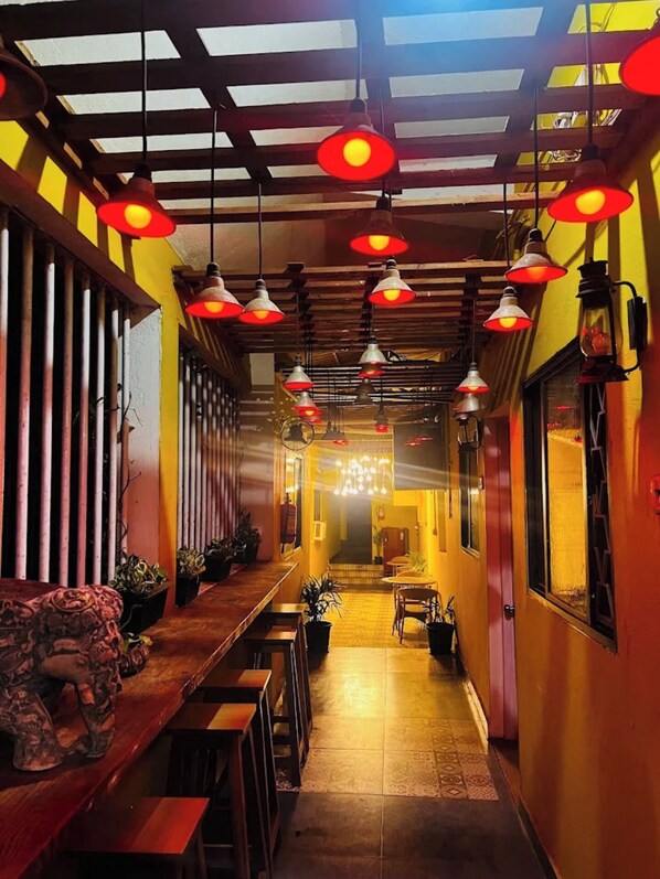 En korridor med hängande röda lampor, träbänkar och krukväxter.