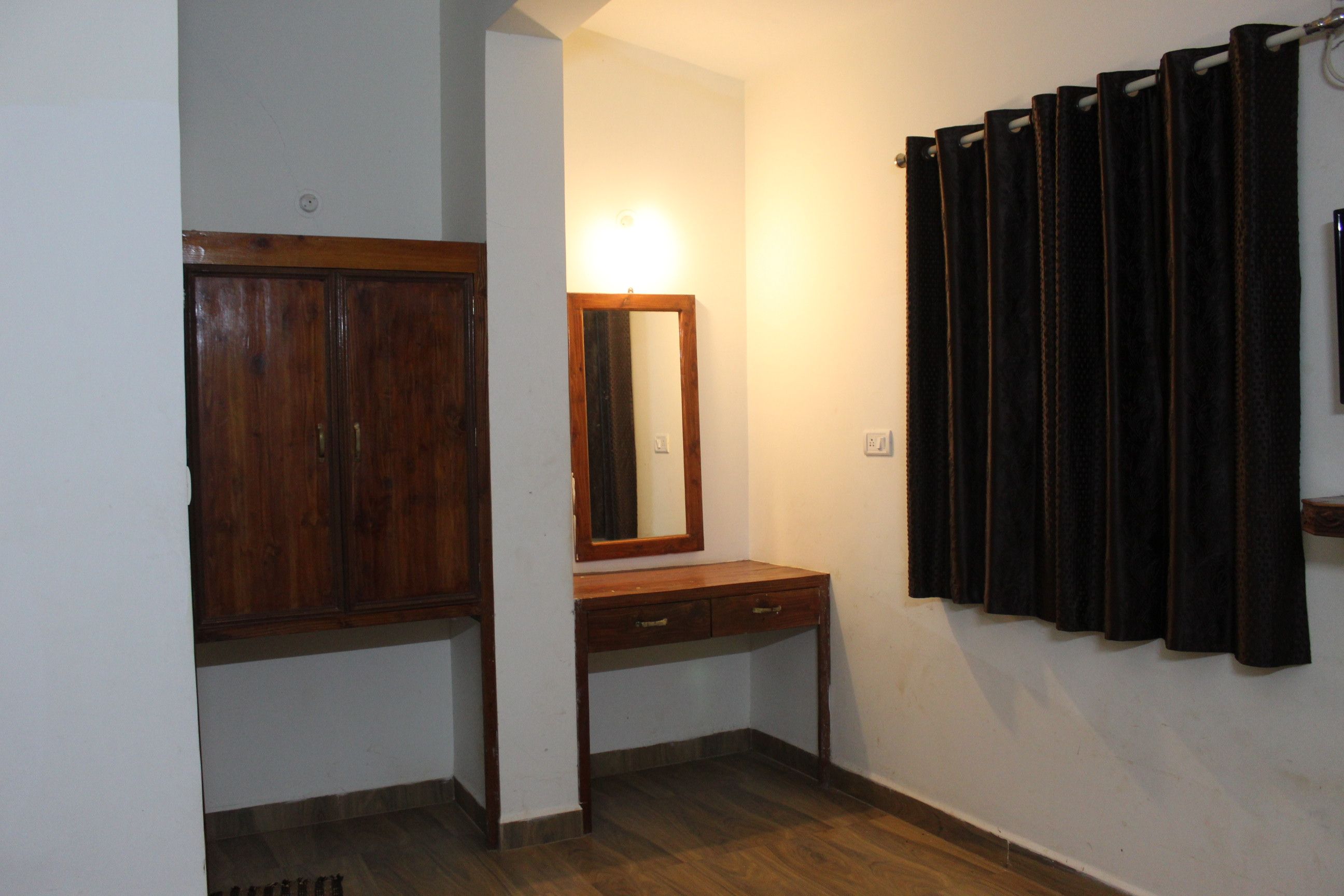 Ein Zimmer mit einem Holzschrank, einem Spiegel über einer Holzkommode und einem Vorhang an der Wand.