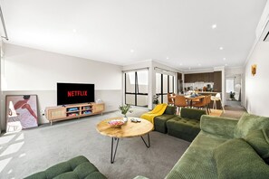 A modern living room with a television, sofa, and a dining area in the background. - Seednest Modern Home, BBQ Balcony & Park Views (Mill Park)