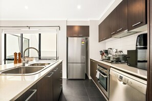 A modern kitchen with stainless steel appliances, wooden cabinets, and a dishwasher. - Seednest Modern Home, BBQ Balcony & Park Views (Mill Park)