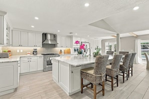 A spacious kitchen with a central island, modern appliances, and a dining area with wicker chairs. - The Windquest Inn 3B / 3.5B + Den Private Canal Home by RVA (Longboat Key)