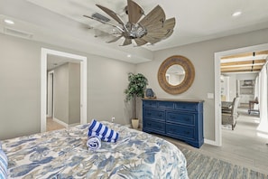 A bedroom with a large bed, a ceiling fan, a dresser, a mirror, and a plant. - The Windquest Inn 3B / 3.5B + Den Private Canal Home by RVA (Longboat Key)