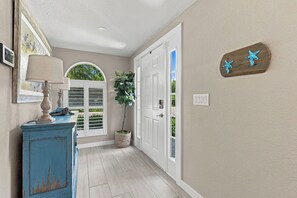 A hallway with a wooden cabinet, a potted plant, and a door with a window. - The Windquest Inn 3B / 3.5B + Den Private Canal Home by RVA (Longboat Key)