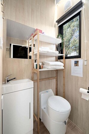 A compact bathroom with a white sink, a toilet, and a wooden shelf unit with towels.
