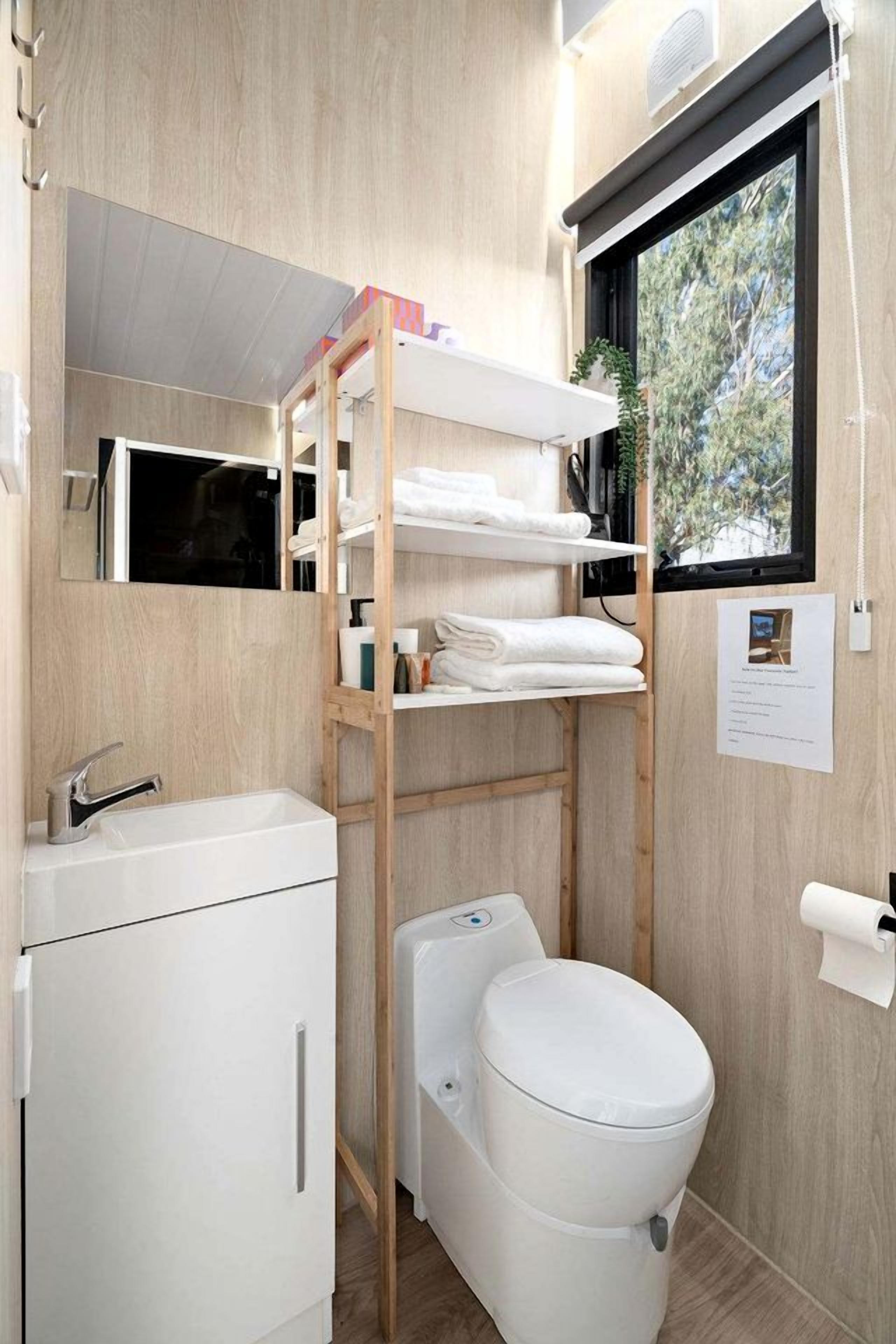 Une petite salle de bain avec un lavabo blanc, des toilettes et une étagère en bois où sont rangées des serviettes.
