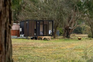 A small cabin with a sliding door, a table, and a fire pit in a wooded area.