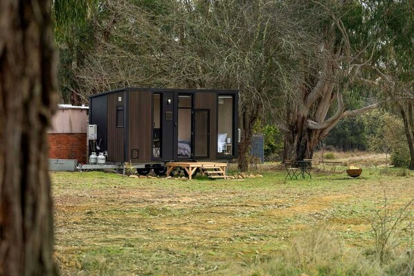 Una cabaña pequeña con puerta corredera, una mesa y un hogar en un área boscosa.