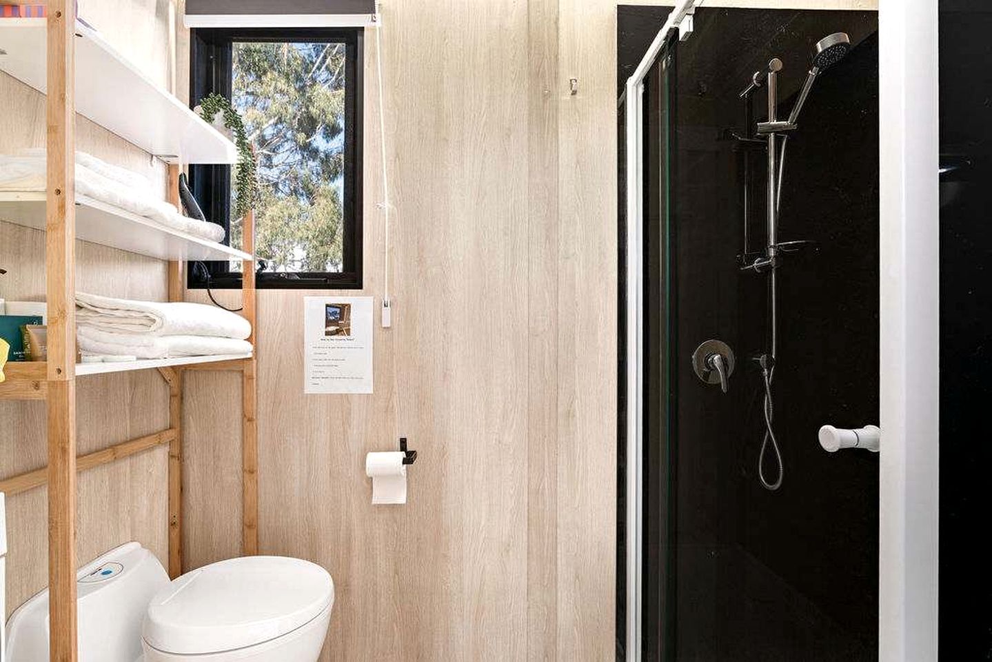 Une petite salle de bain comprenant des toilettes, une étagère avec des serviettes, une fenêtre et un espace douche.