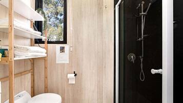 Une petite salle de bain comprenant des toilettes, une étagère avec des serviettes, une fenêtre et un espace douche.