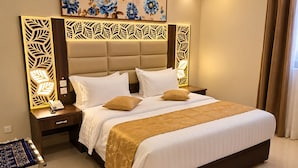 Quarto de hotel com uma cama grande, mesa de cabeceira com telefone, cabeceira decorativa e um quadro na parede.
