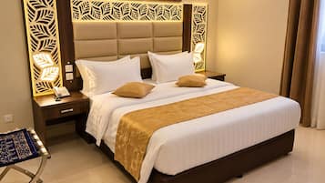 A hotel room with a large bed, a bedside table with a phone, a decorative headboard, and a painting on the wall.