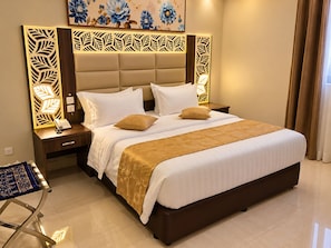 A hotel room with a large bed, a bedside table with a phone, a decorative headboard, and a painting on the wall. - Manazelna serviced apartments- economic (Jeddah)