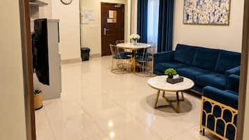 Una sala de estar moderna con un sofá azul, una mesa de centro redonda y una zona de comedor con una mesa y sillas blancas.