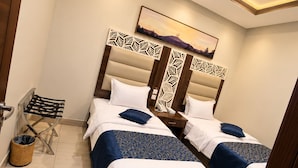 Quarto de hotel com duas camas, cabeceira de madeira, telefone fixado na parede, lixeira pequena e uma imagem de montanhas.