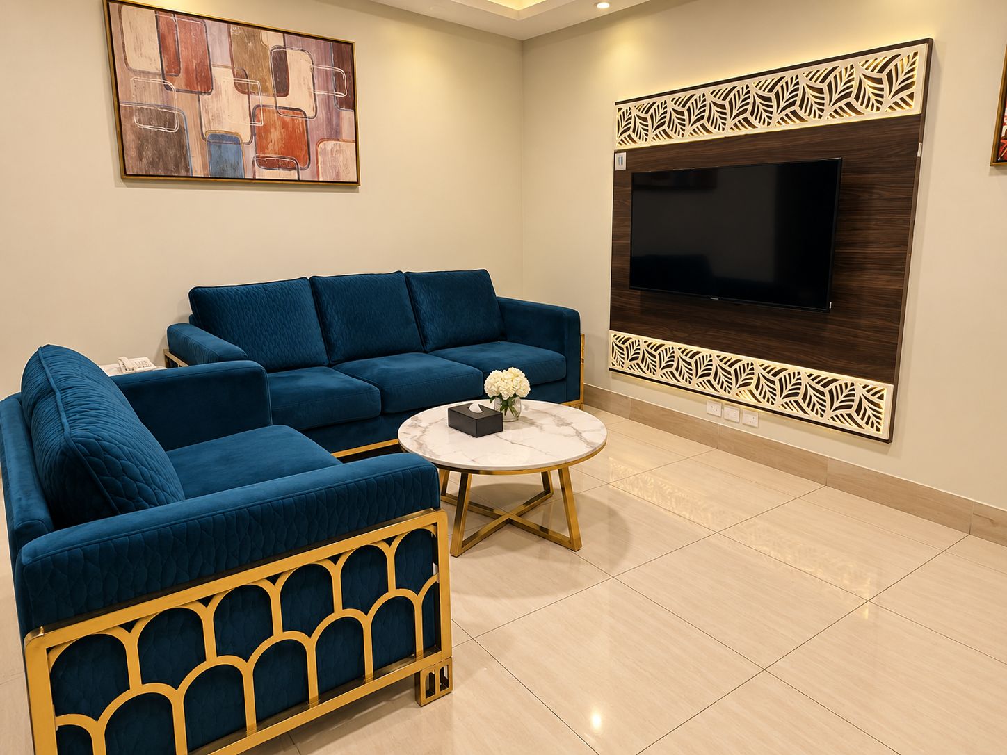 A living room with a blue sofa, a round coffee table, and a flat-screen TV mounted on a decorative panel.