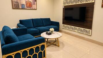A living room with a blue sofa, a round coffee table, and a flat-screen TV mounted on a decorative panel.