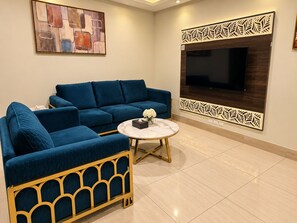 Una sala de estar con un sofá azul, una mesa de centro redonda y un televisor de pantalla plana montado en un panel decorativo.