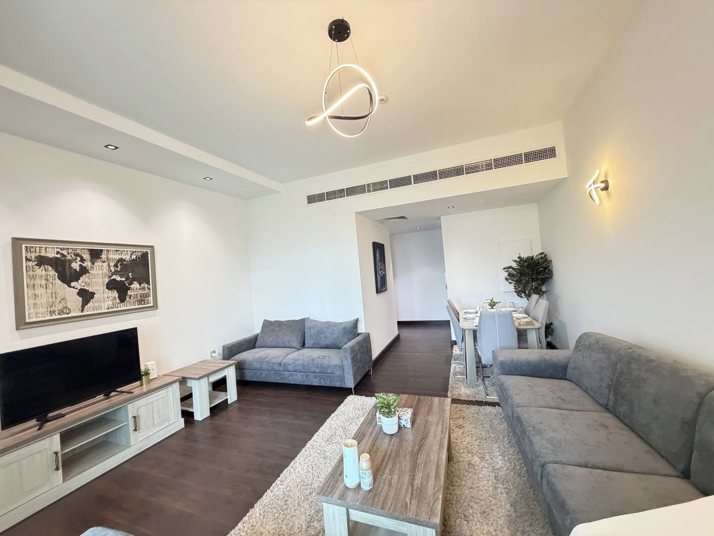 A modern living room with a flat-screen TV, grey sofas, a coffee table, and a world map artwork on the wall.