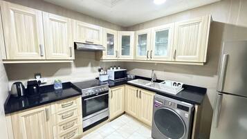 A compact kitchen with light wood cabinets, a stainless steel stove, a microwave, a sink, and a built-in washing machine.