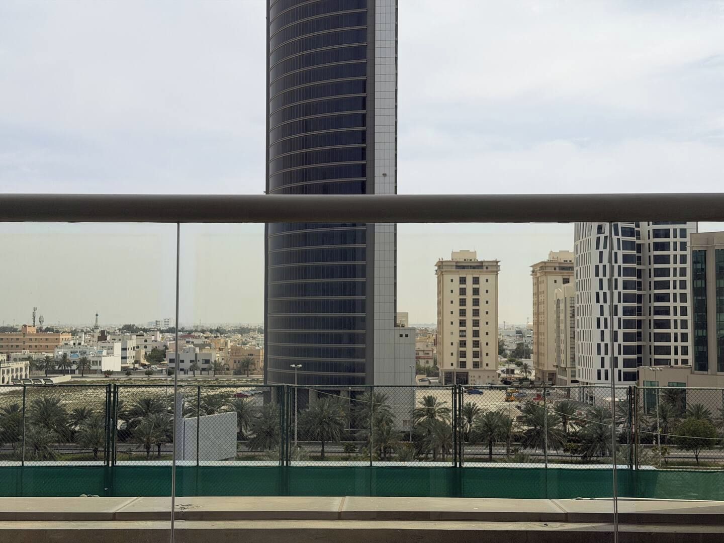 A view of a cityscape with tall buildings, including a prominent cylindrical skyscraper, from behind a safety railing.