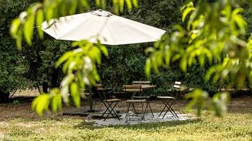 Un espace extérieur aménagé avec une table et des chaises, protégé par un grand parasol et entouré de verdure.