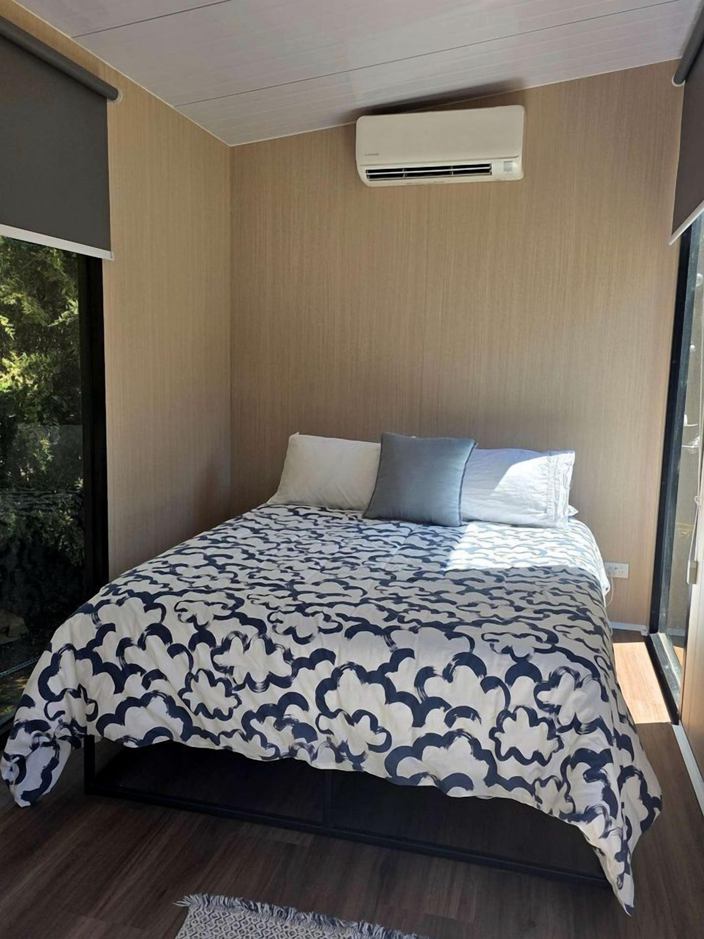 A modern bedroom with a bed, a window, and an air conditioning unit.