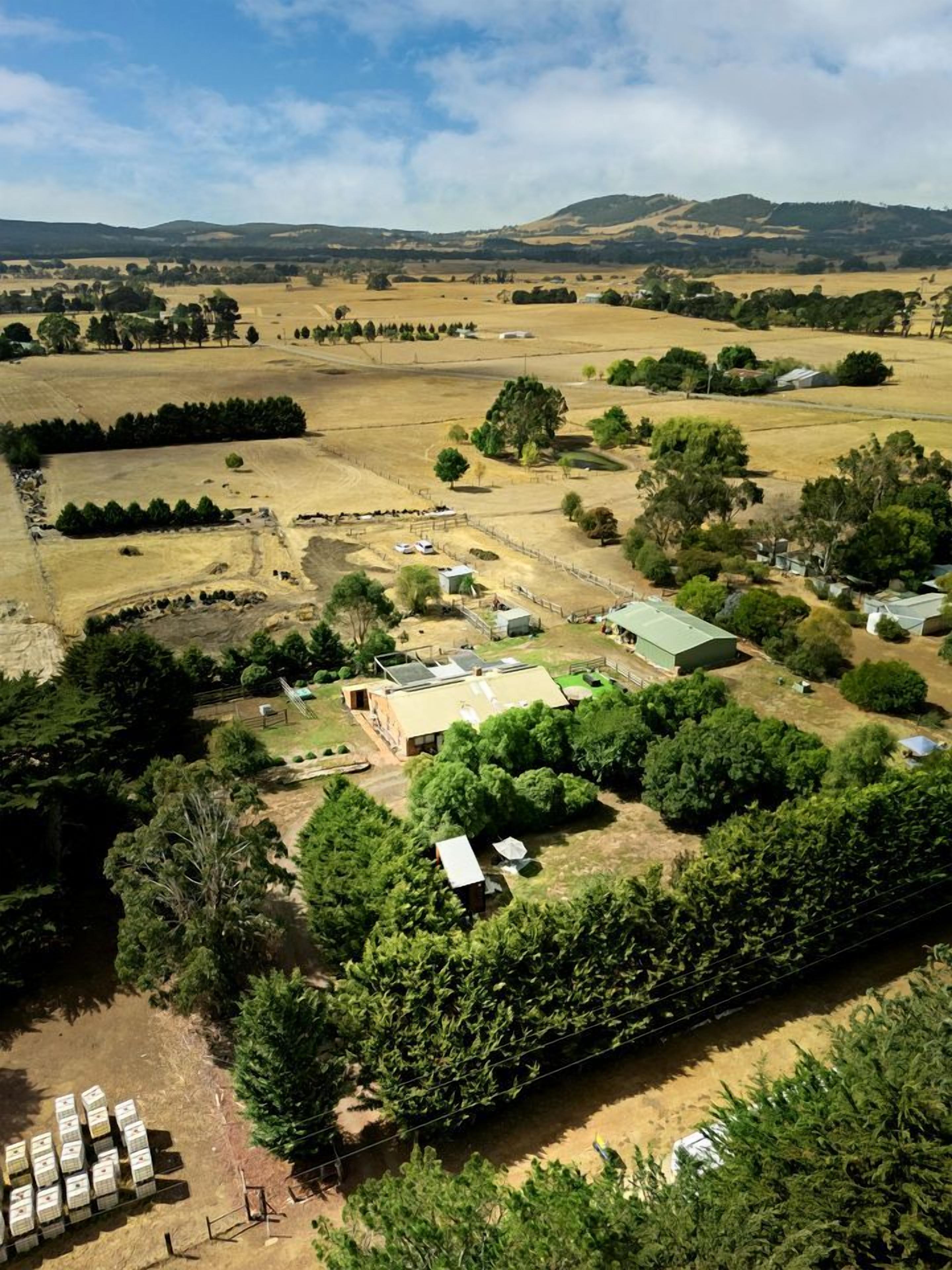 An aerial view of a rural property with a farmhouse, open fields, and scattered trees.