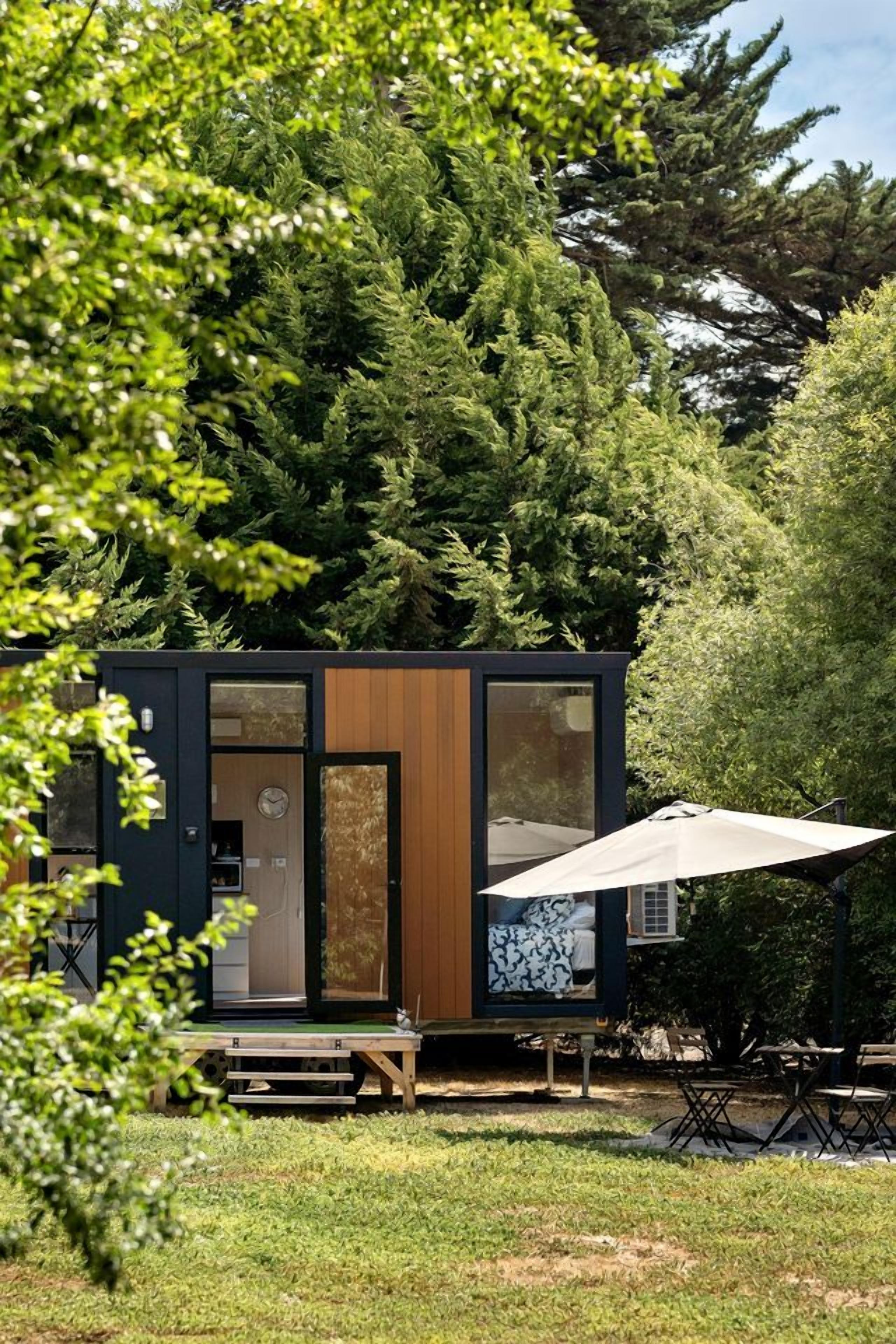 A modern cabin with a wooden door, a visible clock, and a patio area with a table and chairs.