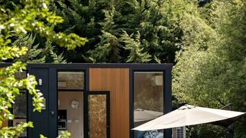 A modern cabin with a wooden door, a visible clock, and a patio area with a table and chairs.