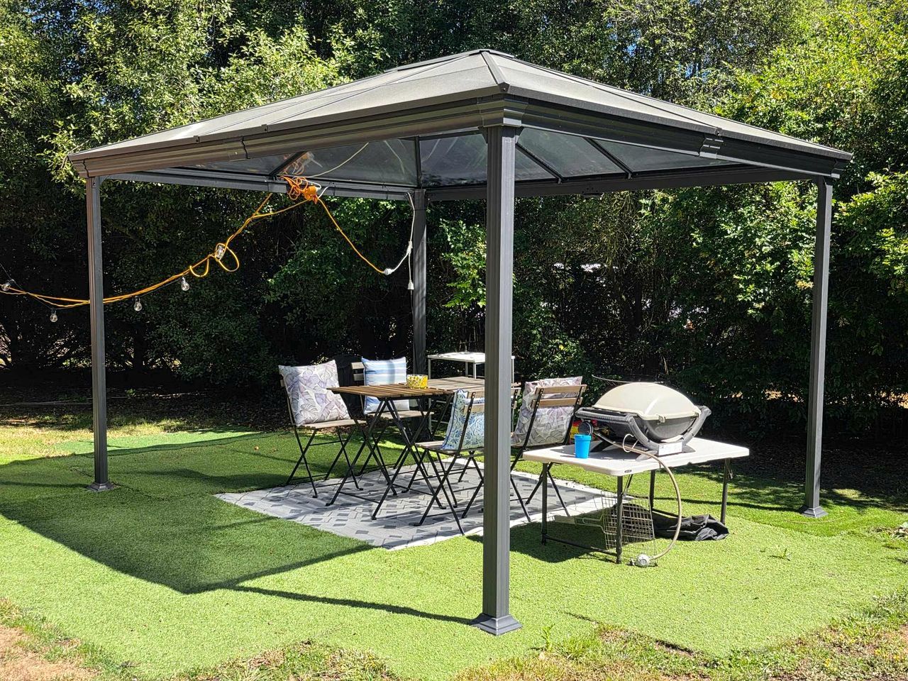 Un espacio al aire libre cubierto con una mesa, sillas, una parrilla y un generador eléctrico.