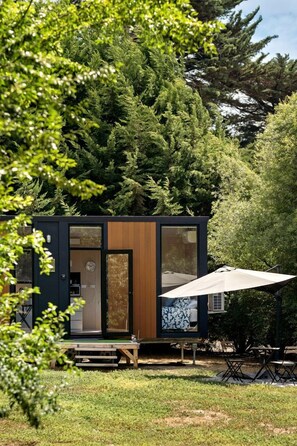 A modern cabin with a wooden door, a visible clock, and a patio area with a table and chairs.