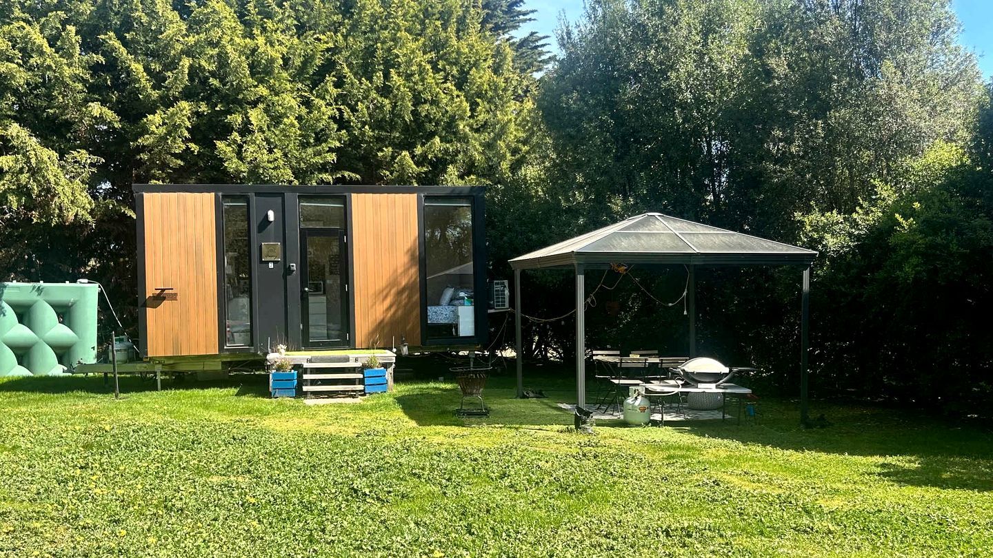 Un espace de vie extérieur moderne, doté d’une structure en bois, d’un patio couvert et d’une pelouse.