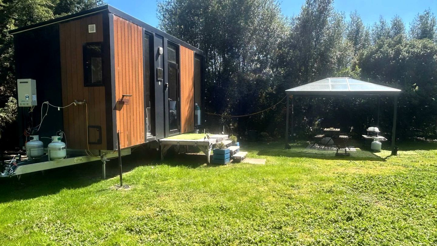 Una casa móvil con un espacio exterior techado, una parrilla y tanques de propano.