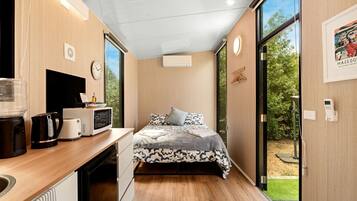 A compact room with a bed, a desk with a kettle, a microwave, and a large window.