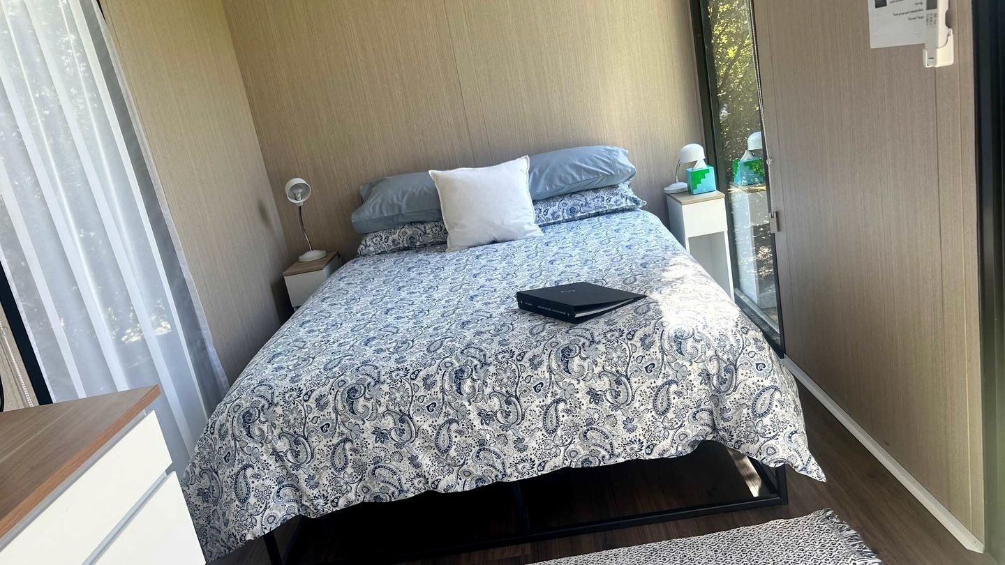 Un dormitorio con cama, mesitas de noche, una lámpara y un ventanal.