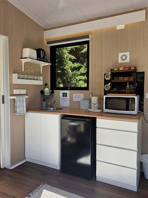 A compact kitchen with a dishwasher, a microwave, and a window with a view of greenery.
