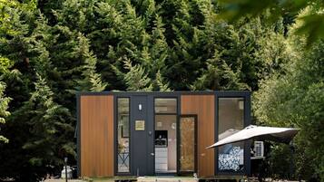 Una cabaña moderna con fachada de madera, puerta de cristal y un patio con mesa y sombrilla.
