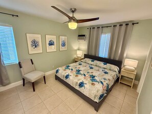 A bedroom with a bed, a chair, a ceiling fan, and framed artwork on the wall. - Pompano Vibes Beach Apartments - Unit 2 "Coral Reef" (Pompano Beach)